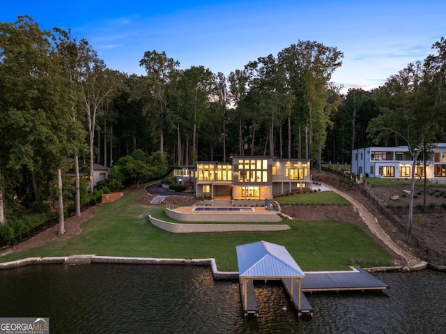 back house at dusk featuring a water view and a lawn