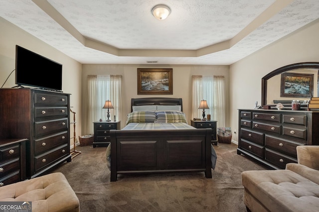 bedroom with a tray ceiling, dark carpet, and a textured ceiling