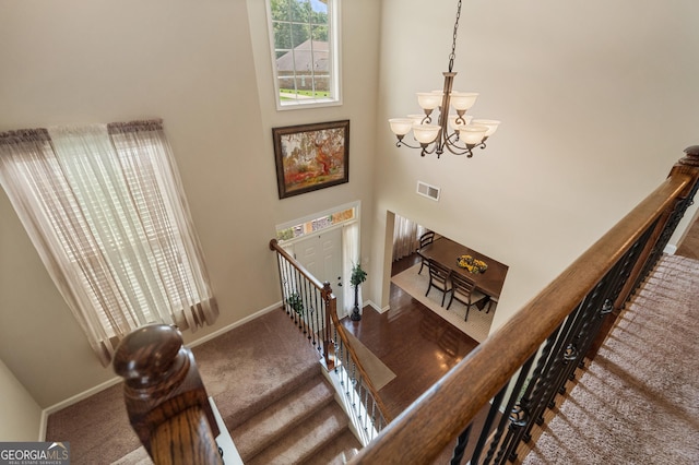 staircase with a towering ceiling, carpet floors, and a notable chandelier