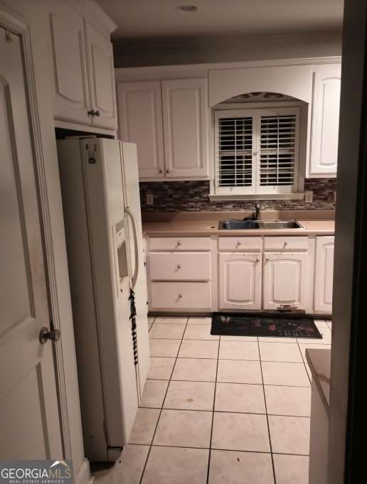 kitchen with white cabinetry, light tile patterned floors, sink, and white fridge with ice dispenser