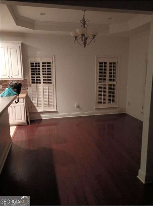 unfurnished dining area featuring dark hardwood / wood-style floors, a tray ceiling, and a notable chandelier