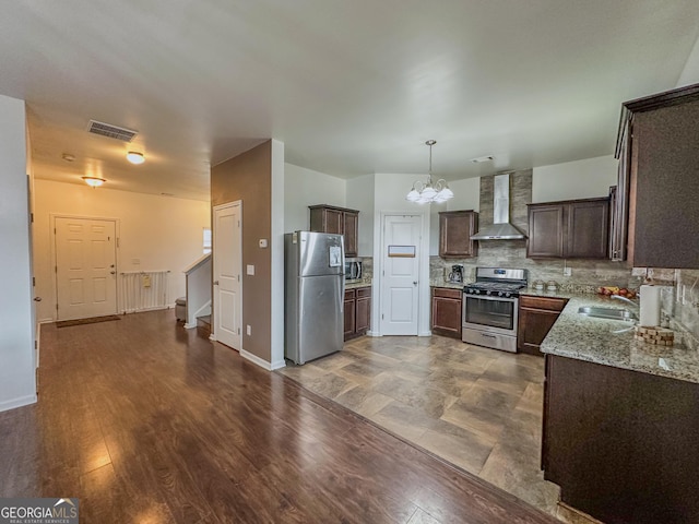 kitchen with appliances with stainless steel finishes, dark brown cabinets, light stone counters, tasteful backsplash, and wall chimney exhaust hood