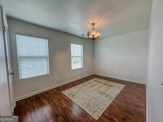 empty room featuring an inviting chandelier and dark hardwood / wood-style flooring