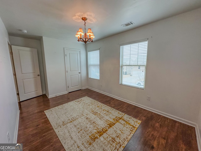 empty room with dark hardwood / wood-style flooring and a chandelier