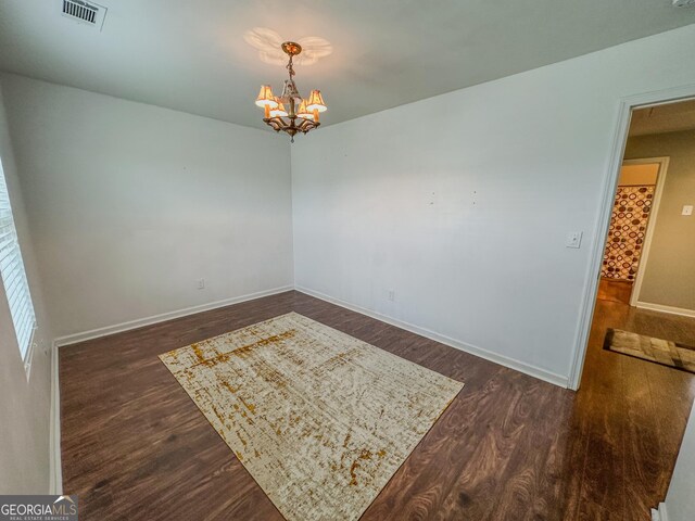 empty room with dark wood-type flooring and a chandelier