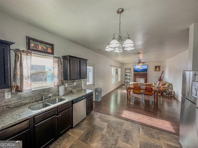 kitchen with sink, appliances with stainless steel finishes, dark brown cabinets, light stone countertops, and decorative light fixtures