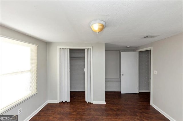 unfurnished bedroom featuring multiple windows, dark hardwood / wood-style floors, and a textured ceiling