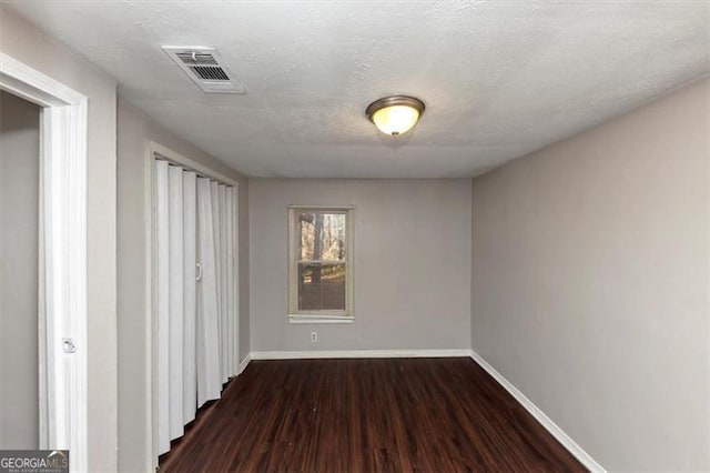 empty room with dark hardwood / wood-style floors and a textured ceiling