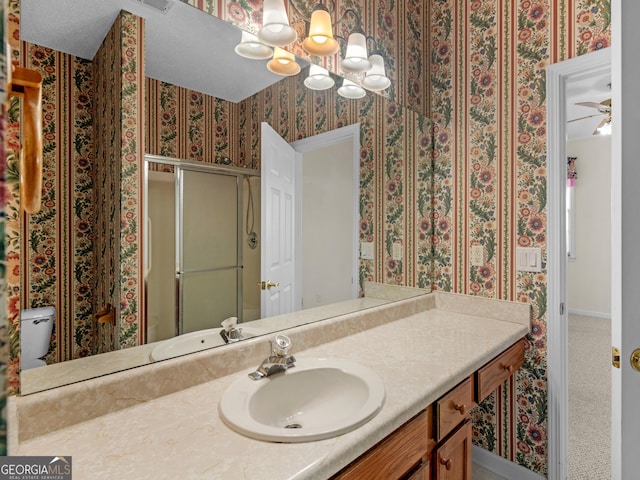 bathroom with vanity, ceiling fan with notable chandelier, toilet, and walk in shower