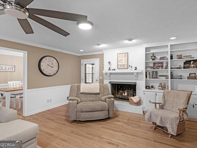 living room featuring ornamental molding, ceiling fan, a brick fireplace, a textured ceiling, and light hardwood / wood-style flooring