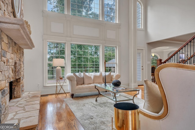 living room with light hardwood / wood-style flooring, a towering ceiling, a fireplace, and plenty of natural light