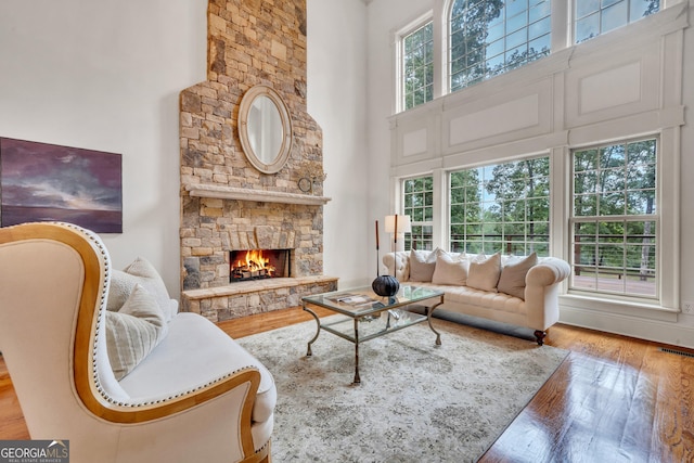 living room featuring a towering ceiling, wood-type flooring, and a stone fireplace