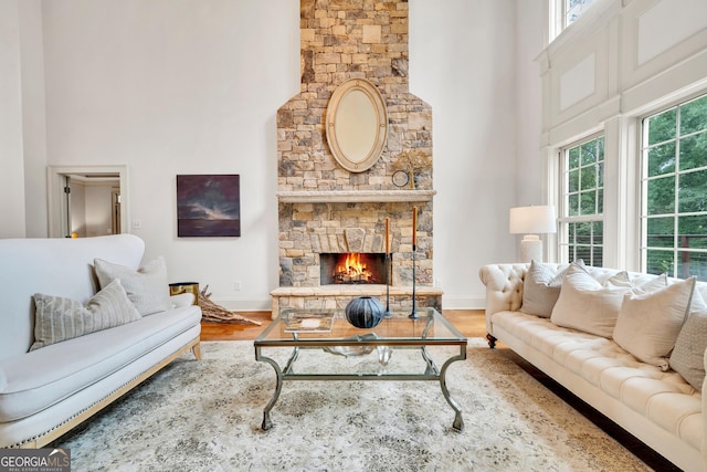 living room featuring hardwood / wood-style floors, a stone fireplace, plenty of natural light, and a high ceiling