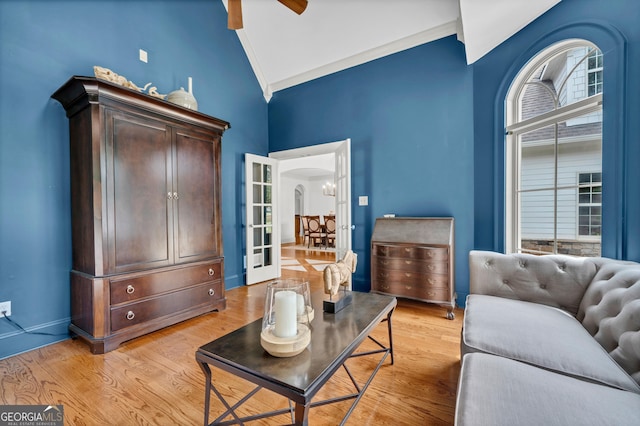 interior space featuring high vaulted ceiling, ornamental molding, ceiling fan with notable chandelier, french doors, and light wood-type flooring