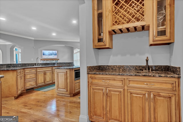 kitchen with sink, stainless steel microwave, ornamental molding, dark stone counters, and light wood-type flooring