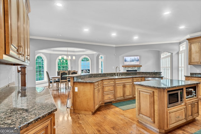 kitchen with stainless steel microwave, sink, crown molding, and a center island with sink