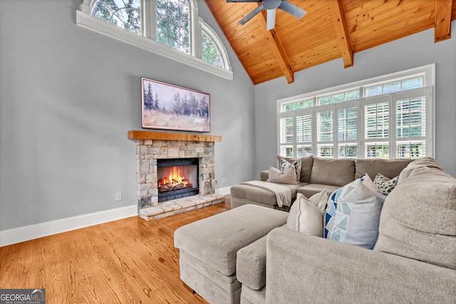 living room with a wealth of natural light, a stone fireplace, beam ceiling, and wooden ceiling