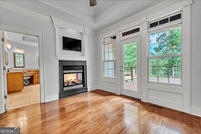 doorway with ceiling fan, a multi sided fireplace, ornamental molding, and light hardwood / wood-style floors