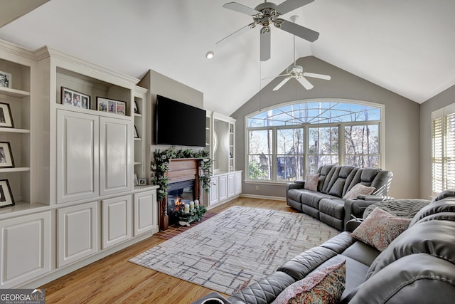 living room with built in shelves, lofted ceiling, a tiled fireplace, and light hardwood / wood-style floors