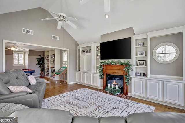 living room with hardwood / wood-style floors, built in shelves, high vaulted ceiling, and ceiling fan