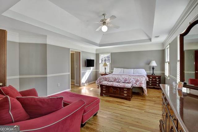 bedroom with a tray ceiling, ornamental molding, ceiling fan, and light wood-type flooring