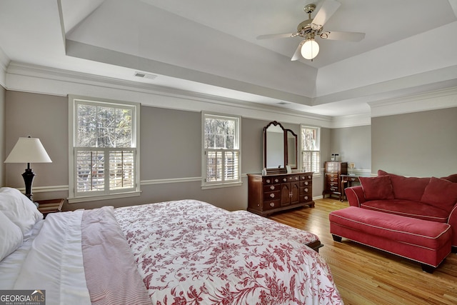 bedroom with hardwood / wood-style flooring, ceiling fan, crown molding, and a raised ceiling