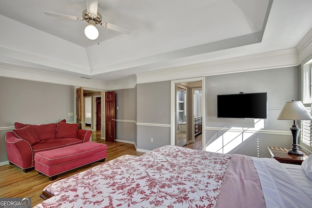 bedroom with hardwood / wood-style flooring, ornamental molding, ceiling fan, and a tray ceiling