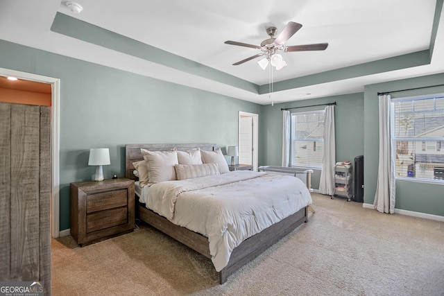 bedroom featuring ceiling fan, a tray ceiling, and light colored carpet