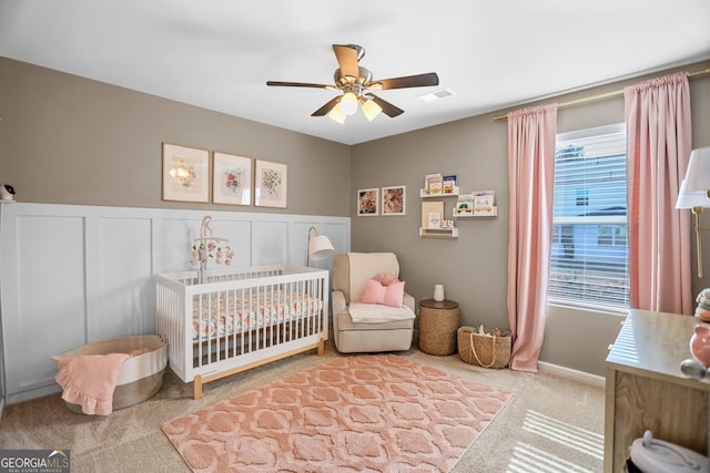 carpeted bedroom featuring a crib and ceiling fan