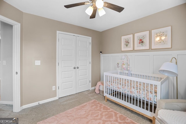 carpeted bedroom with a nursery area, ceiling fan, and a closet