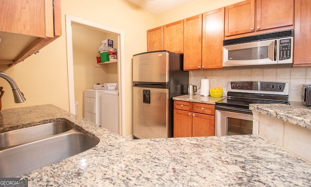 kitchen featuring appliances with stainless steel finishes, separate washer and dryer, sink, backsplash, and light stone counters