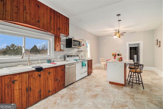 kitchen with a breakfast bar, sink, appliances with stainless steel finishes, a kitchen island, and ceiling fan