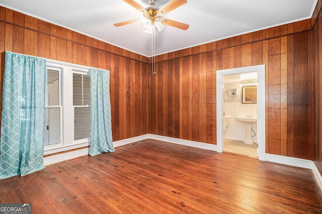 unfurnished room featuring crown molding, hardwood / wood-style floors, ceiling fan, and wood walls