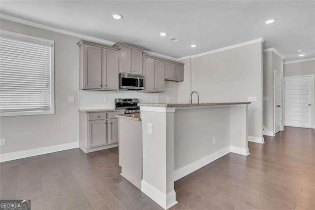 kitchen featuring dark wood-type flooring, gray cabinetry, crown molding, a center island with sink, and appliances with stainless steel finishes