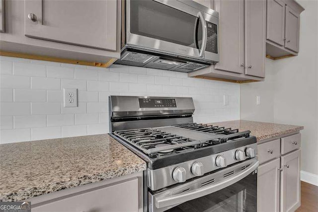 kitchen with appliances with stainless steel finishes, dark hardwood / wood-style floors, gray cabinetry, backsplash, and light stone countertops