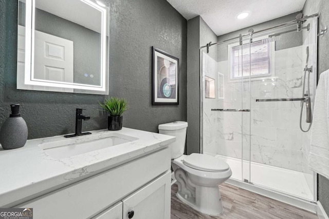 bathroom featuring toilet, a shower with shower door, wood-type flooring, a textured ceiling, and vanity