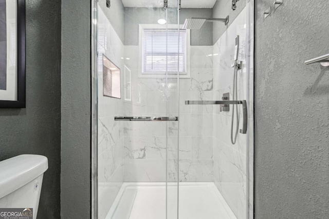 bathroom featuring a shower with door and toilet