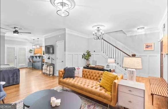 living room with ornamental molding, ceiling fan with notable chandelier, and light wood-type flooring