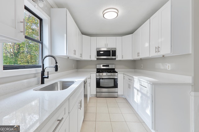 kitchen with sink, white cabinetry, light tile patterned floors, appliances with stainless steel finishes, and light stone countertops