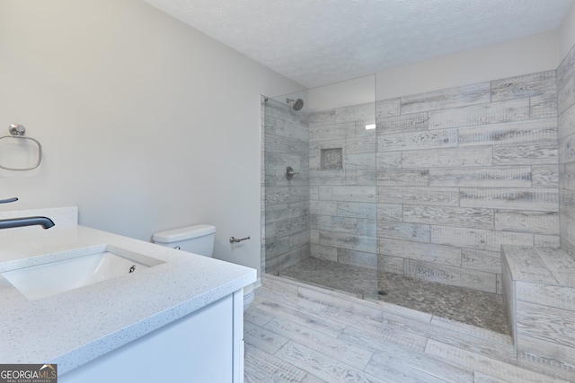 bathroom featuring wood-type flooring, vanity, tiled shower, toilet, and a textured ceiling