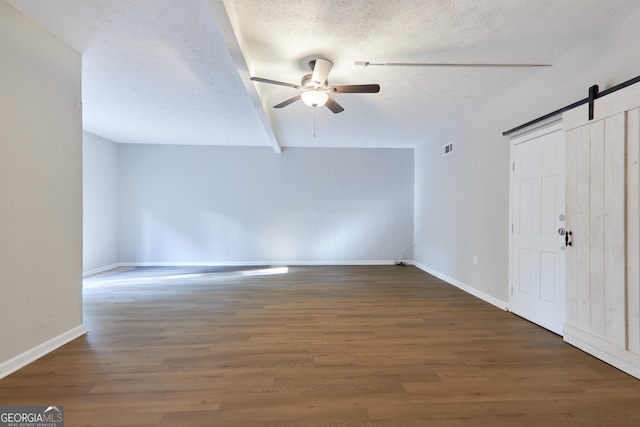 interior space featuring dark wood-type flooring, ceiling fan, a barn door, and a textured ceiling