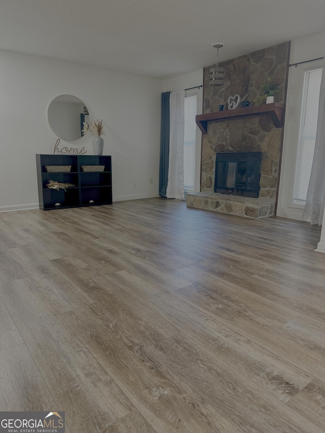unfurnished living room featuring a stone fireplace, baseboards, and wood finished floors
