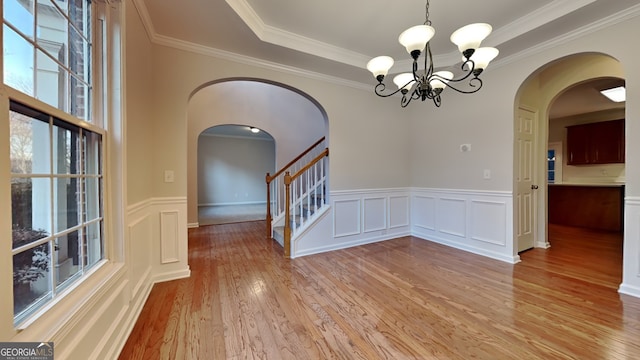 unfurnished dining area featuring crown molding, a chandelier, a raised ceiling, and light hardwood / wood-style flooring