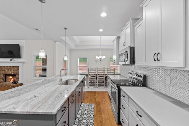 kitchen featuring sink, appliances with stainless steel finishes, hanging light fixtures, white cabinets, and a large island with sink