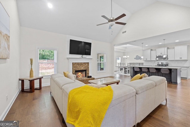 living room with sink, high vaulted ceiling, a brick fireplace, dark hardwood / wood-style flooring, and ceiling fan