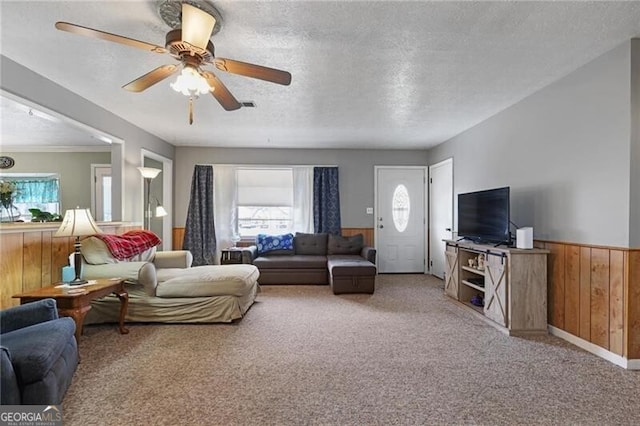 carpeted living room with ceiling fan, a textured ceiling, and wooden walls