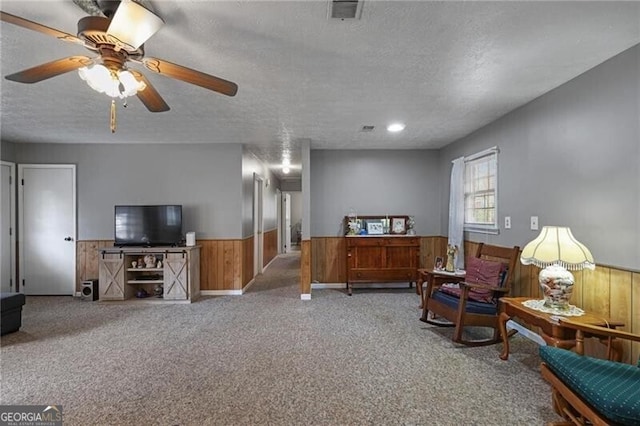 living area with ceiling fan, light colored carpet, a textured ceiling, and wood walls