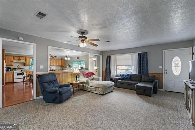 living room featuring a wealth of natural light, wooden walls, ceiling fan, and carpet