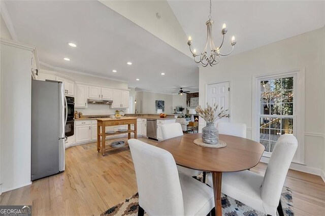 dining room with ceiling fan with notable chandelier, vaulted ceiling, and light hardwood / wood-style floors