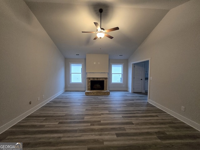 unfurnished living room with dark wood-type flooring, ceiling fan, lofted ceiling, and a brick fireplace